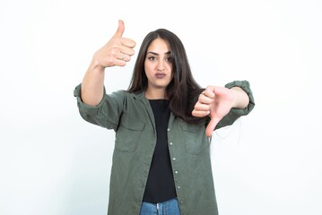 young brunette woman wearing casual clothes over white studio background showing thumbs up and thumbs down, difficult choose concept - obrazy, fototapety, plakaty