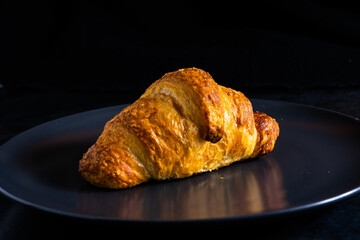 Freshly backed french croissant shiny in the rays of the morning sun, dark background, kitchen