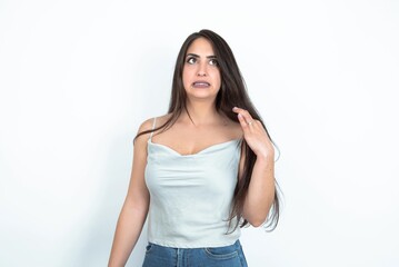 Fototapeta premium young brunette woman wearing white tank top over white studio background stressed, anxious, tired and frustrated, pulling shirt neck, looking frustrated with problem