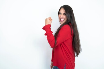 Profile side view portrait Young brunette woman wearing red shirt over white studio background celebrates victory