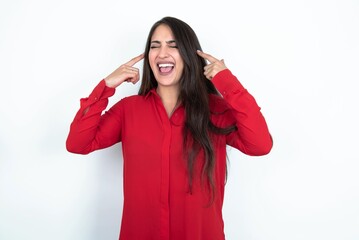 Photo of crazy Young brunette woman wearing red shirt over white studio background screaming and pointing with fingers at hair closed eyes