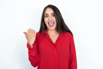 Impressed Young brunette woman wearing red shirt over white studio background point back empty space