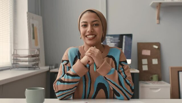 Waist up POV of young Muslim woman having job interview in modern IT office, smiling and chatting at camera