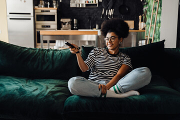 Cheerful african woman watching TV while sitting on couch
