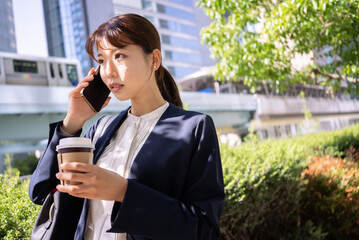 コーヒーを片手にスマホで電話をする日本人ビジネスウーマン