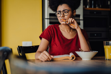 Fototapeta na wymiar African woman studying while having breakfast in kitchen