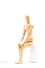 Depressed and sad dummy sitting on a bottle of pills on a white background. Concept of depression