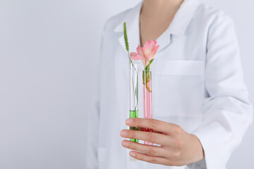 Woman holds test tubes with flower against light background