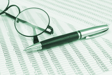 Round eyeglasses and metallic pen on financial reports papers. 