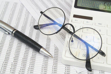 Modern calculator, black glasses and pen on financial papers. Business analytics and paperwork concept.