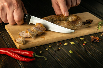 Cutting homemade sausage on a kitchen cutting board with a knife in the chef hand. The national dish is prepared with spices on holidays.
