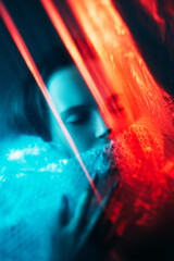 Ghost spirit. Soul silence. Dream mystery. Red blue color light defocused tranquil cold woman face with closed eyes wrapped in polyethylene plastic film on dark.