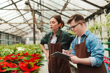 Man with down syndrome writing down notes while woman helping him to handle with flowers in...