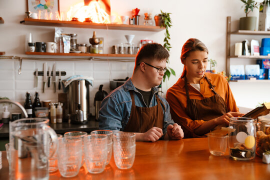 Woman teaching man with down syndrome how to use tablet during internship in cafe