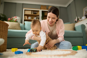 Joyful mother and baby boy playing with toys on a carpet at home