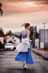 Young tall girl with ponytail in blue sundress and white sweater walking down the street