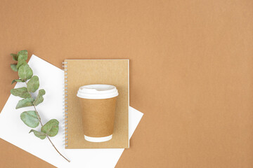 Craft paper coffee cup, notebook and eucalyptus sprig on eco background, flat lay.