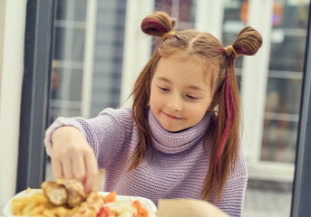 Cute little girl with ponytails eating fast food with hands. Hungry child enjoying fries for lunch in a restaurant