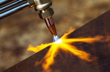Gas cutting of metal. Gas cutter with copper nozzle with a stream of fire directed at the metal....