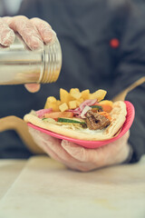 The cook seasoning gyros sandwich with pepper from a shaker. Chef preparing traditional Greek pita souvlaki wrap