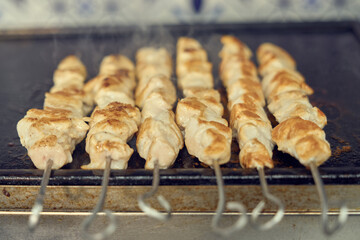Pork meat on metal skewers being cooked in a grill. Traditional Greek fast food preparation