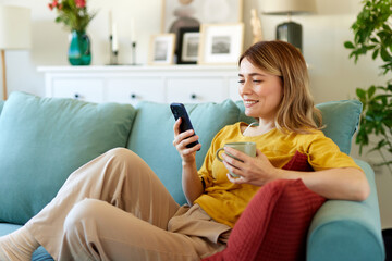 Woman using smartphone while drinking coffee at her home in the morning