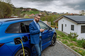 Mature businessman waiting for charging his electric car.