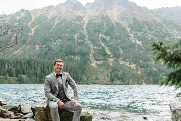 Man on the stony shore. The groom near the lake in the mountains. Groom against the backdrop of a mountain landscape.