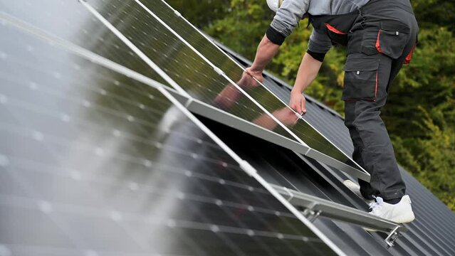 Man technician mounting photovoltaic solar panels on roof of house. Close up view of engineer installing solar module system with help of hex key. Concept of alternative, renewable energy.