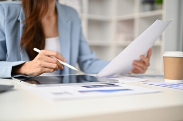 Close-up image of a businesswoman using her tablet while reviewing business report at her desk.