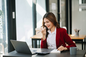 Business asian woman Talking on the phone and using a laptop with a smile while sitting at modern office.
