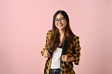 Pretty Asian female college student stands against an isolated pink background.