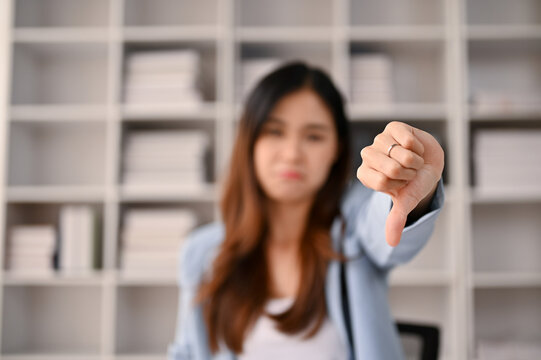 Close-up image of a dissatisfied and upset Asian businesswoman showing thumbs down dislike gesture