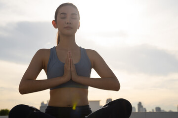 Fototapeta na wymiar Young Asian slim fit woman meditating outdoors in the city
