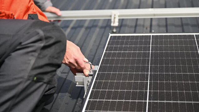 Man technician mounting photovoltaic solar panels on roof of house. Close up engineer installing solar module system with help of hex key. Concept of alternative, renewable energy.