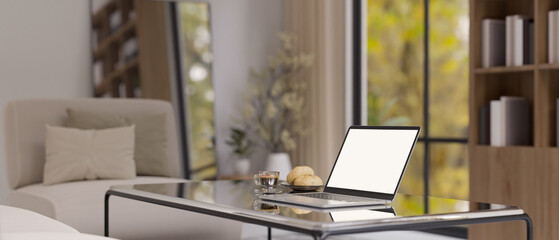 Laptop white screen mockup on a modern coffee table in comfortable living room.