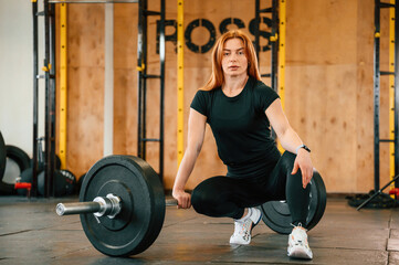 Fototapeta na wymiar Front view. Sitting, barbell on the floor. Beautiful strong woman is in the gym