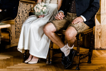 Brautpaar in Tracht mit Dirndl und Lederhose während Trauung hält sich die Hände