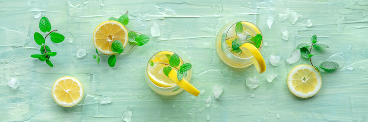 Lemonade with mint panorama. Lemon water drink with ice. Two glasses and lemons on a blue...