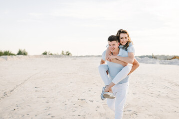 Piggybacking. A handsome young man giving a piggyback ride to a woman in summer sunset. Girl sits...