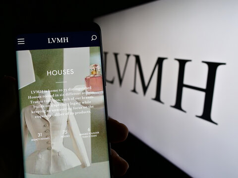 Stuttgart, Germany - 04-16-2023: Person holding cellphone with webpage of company LVMH Moet Hennessy Louis Vuitton SE on screen in front of logo. Focus on center of phone display.