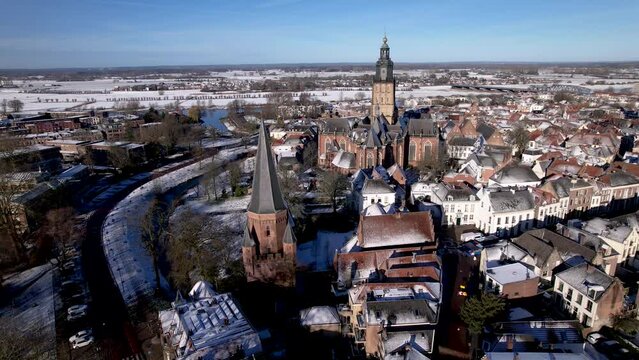 Winter wonderland rooftops covered in snow with aerial approach of Drogenapstoren and historic Hanseatic Dutch tower town Zutphen in The Netherlands with Walburgiskerk cathedral in the background