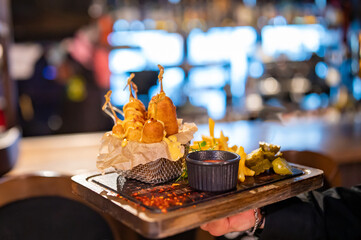 Waiter hold plate with corn dog, french fries and sauce in pub