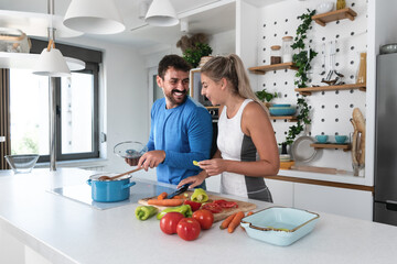 Happy young couple have fun in kitchen while preparing healthy organic food. Beautiful sports...