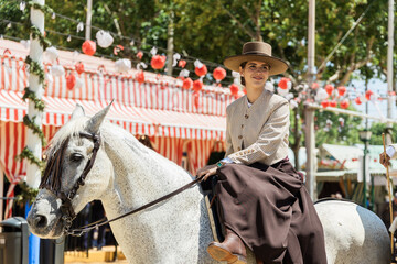Young woman in traditional dress riding a horse at the seville fair - obrazy, fototapety, plakaty