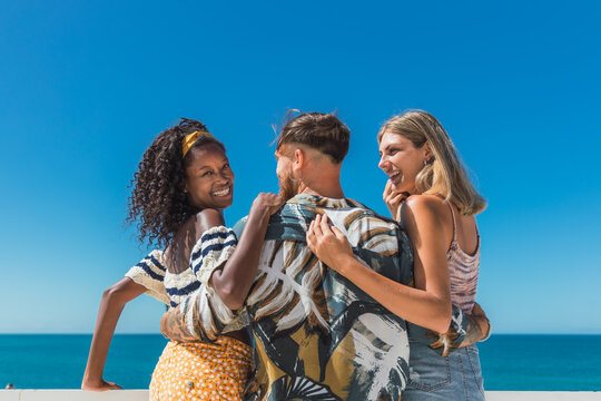 Backview of cheerful black woman with curly hair embracing friends and looking back at camera on balcony with sea view