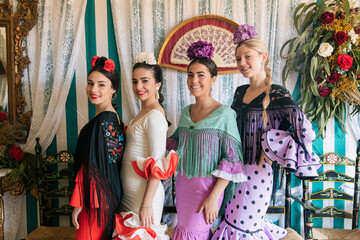 Fototapeta na wymiar Happy women in colorful dresses standing near decorated wall