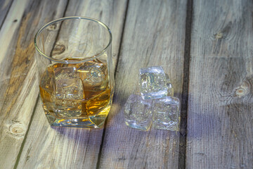 front view of a glass of whiskey with ice on a wooden background with space for writing