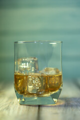 front view of a glass of whiskey with ice on a wooden background 