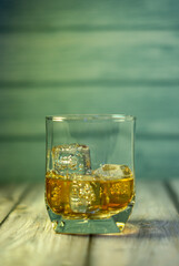 front view of a glass of whiskey with ice on a wooden background